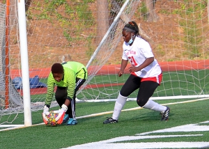 Stone Mountain goalkeeper Manish Kaykez (left) makes one of her six saves in the first half against No. 3 ranked Chamblee. Defensive teammate Maimuna Tamba (21) comes over to help defend. (Photo by Mark Brock)